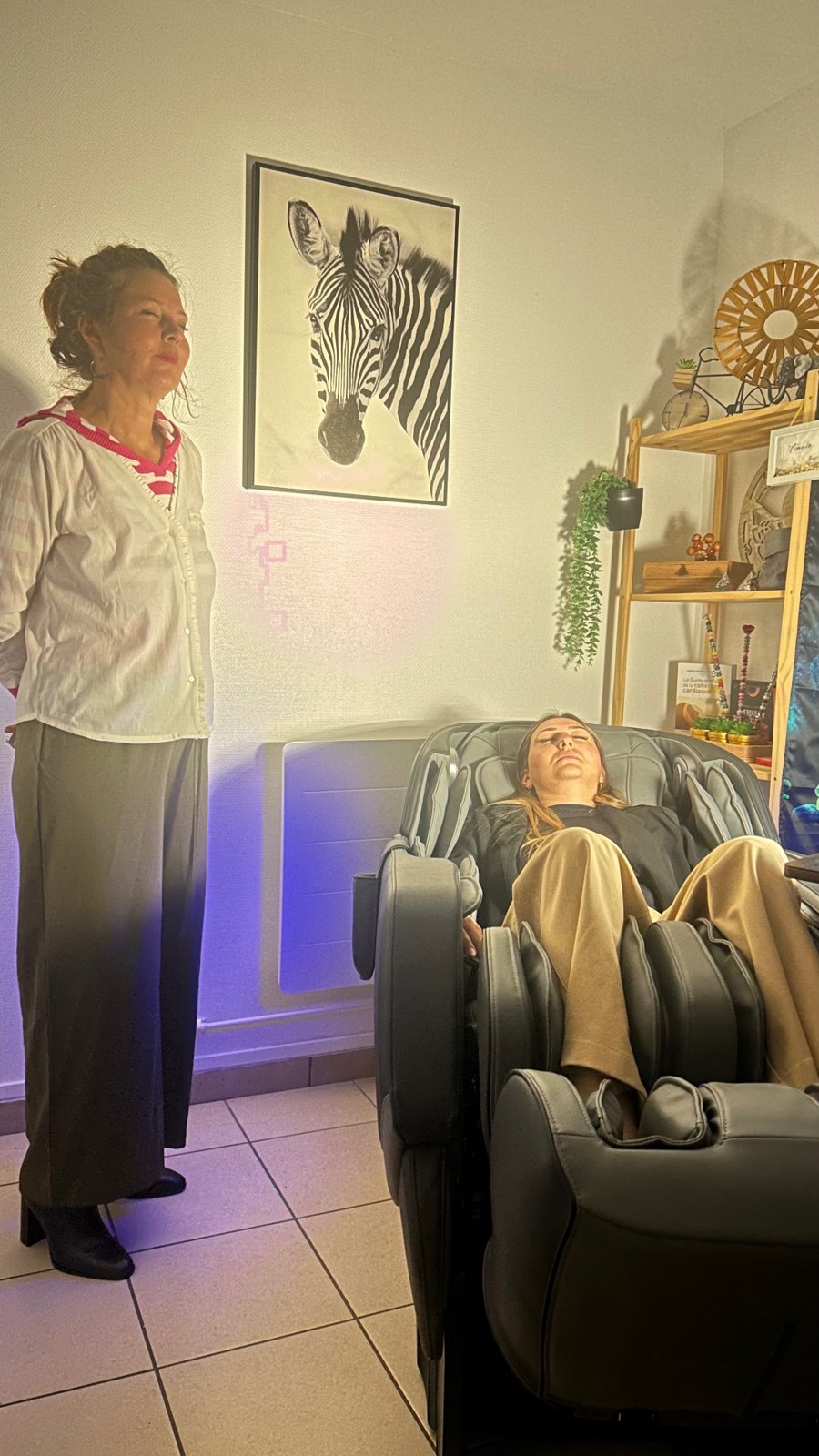 Une personne debout auprès d’une visiteuse installée dans le fauteuil zéro gravité